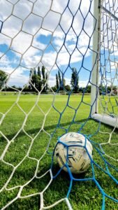 Football resting inside a goal net on a green field